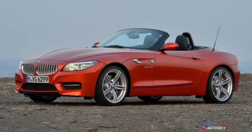 BMW Z4 Roadster luxury convertible car driving along Dubai’s coastal road under sunny weather.